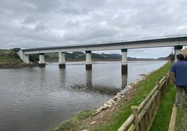 Un hombre pasea junto a la Ría del Eo entre Vegadeo y Castropol, a la vista del puente ferroviario en la zona del horno de cal.