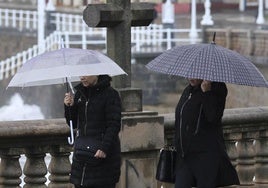 Dos mujeres caminan con paraguas en Gijón.