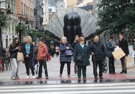 Varias personas llevando bolsas a la altura de la calle en Palacio Valdés de Oviedo.