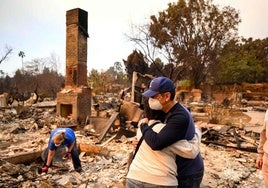 Dos personas se abrazan mientras otra busca objetos entre los escombros causados por los devastadores incendios que asolan Los Ángeles.