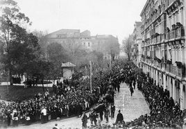 Marzo de 1913. Multitudinario cortejo fúnebre, camino de Ceares, con los ataúdes de los fallecidos en la catástrofe de El Musel a su paso por la esquina de Begoña donde estuvo la plaza de toros de madera. Al fondo se ve la manzana de Dindurra.