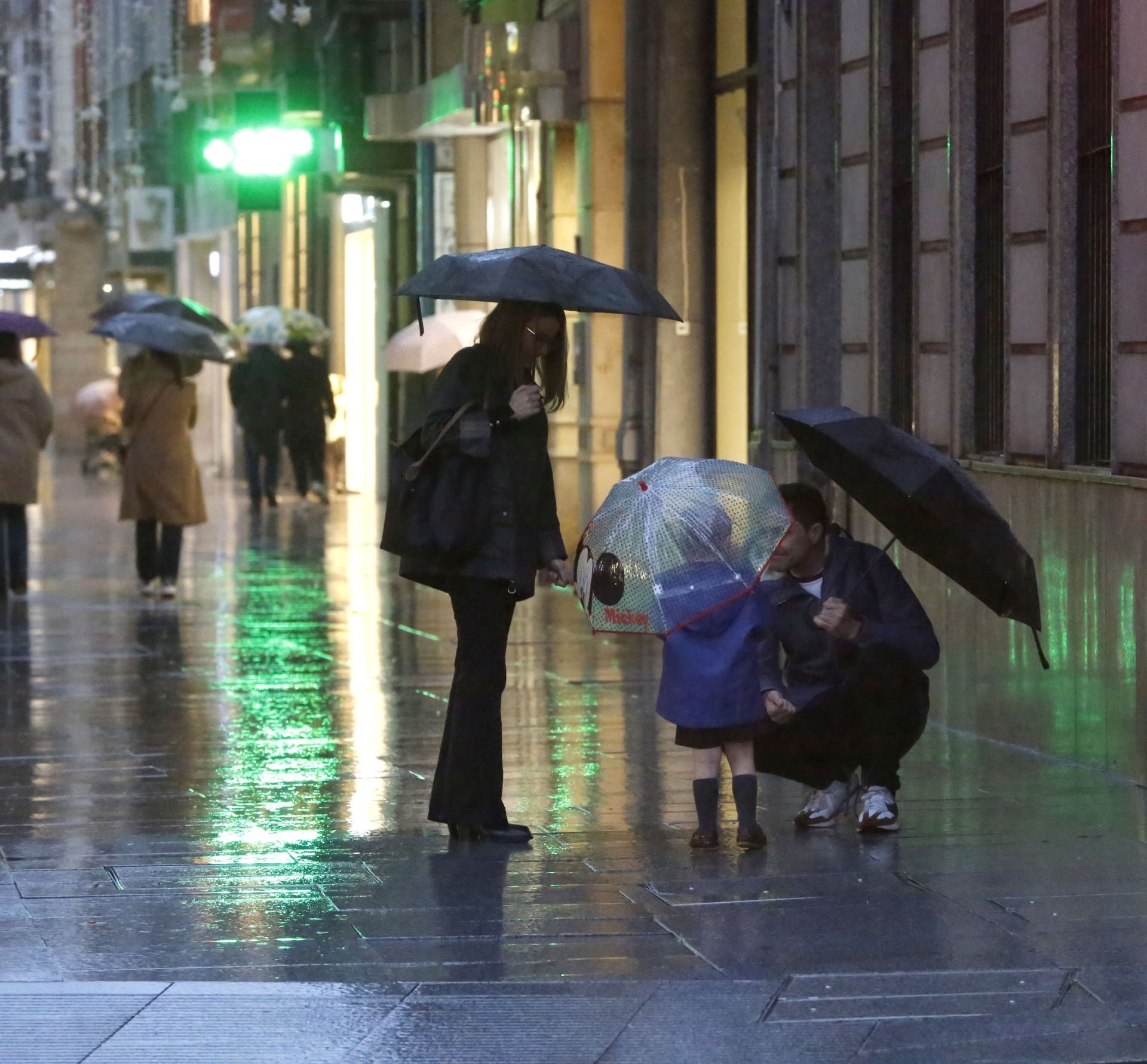 Una familia pasea, bajo la lluvia, por la calle Corrida de Gijón.