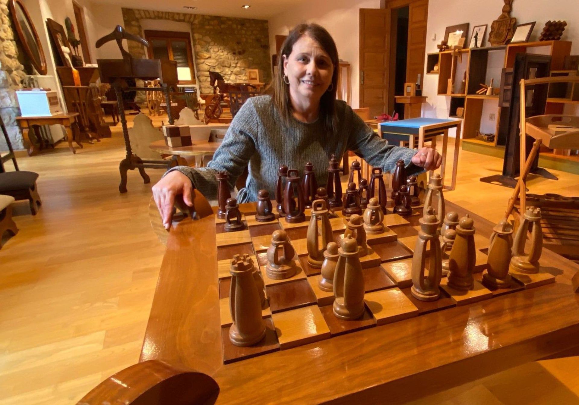 Ana Gloria Fernández Melendreras, con una magnífica y premiada pieza de los alumnos, un ajedrez de primorosa talla en las piezas y con escaques de diferentes alturas, dando una sensación de tres dimensiones muy llamativa. A su espalda, muchas de las piezas en la sala de exposiciones de la planta alta de la Casona del Marqués de Cobián.