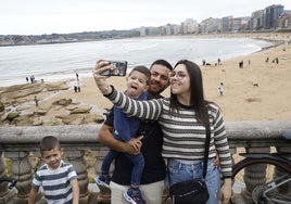 Una familia de turistas se hacen una fotografía desde el Campo Valdés, con la playa de San Lorenzo detrás.