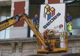 Trabajadores retiran un cartel de la constructora Sedes de un edificio de Oviedo.