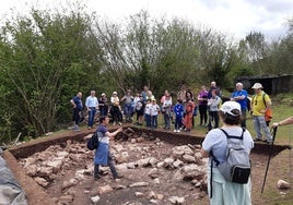 El arqueólogo Juan Ramón Muñiz explica detalles del castro de Pico Castiello a los vecinos. A sus pies, los restos descubiertos de una cabaña prerromana