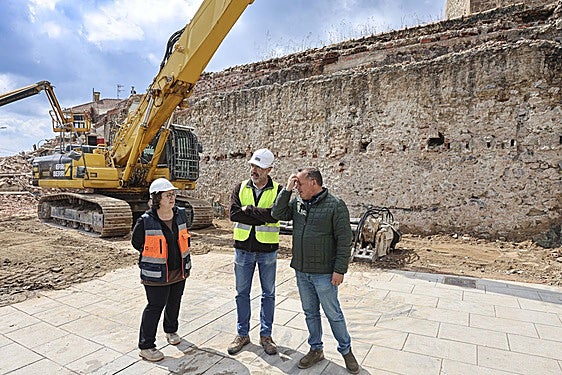 Noelia Fernández y Alejandro García conversan con el concejal Pelayo García ante un tramo de muralla descubierto.