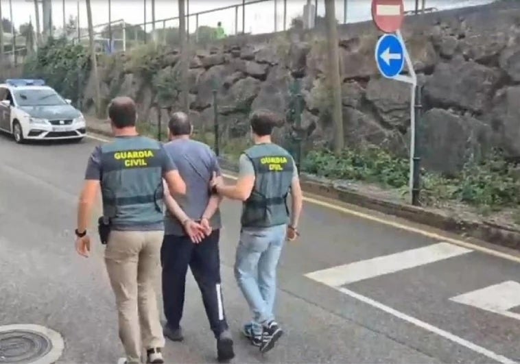Dos agentes de la Guardia Civil trasladan al detenido al coche policial.