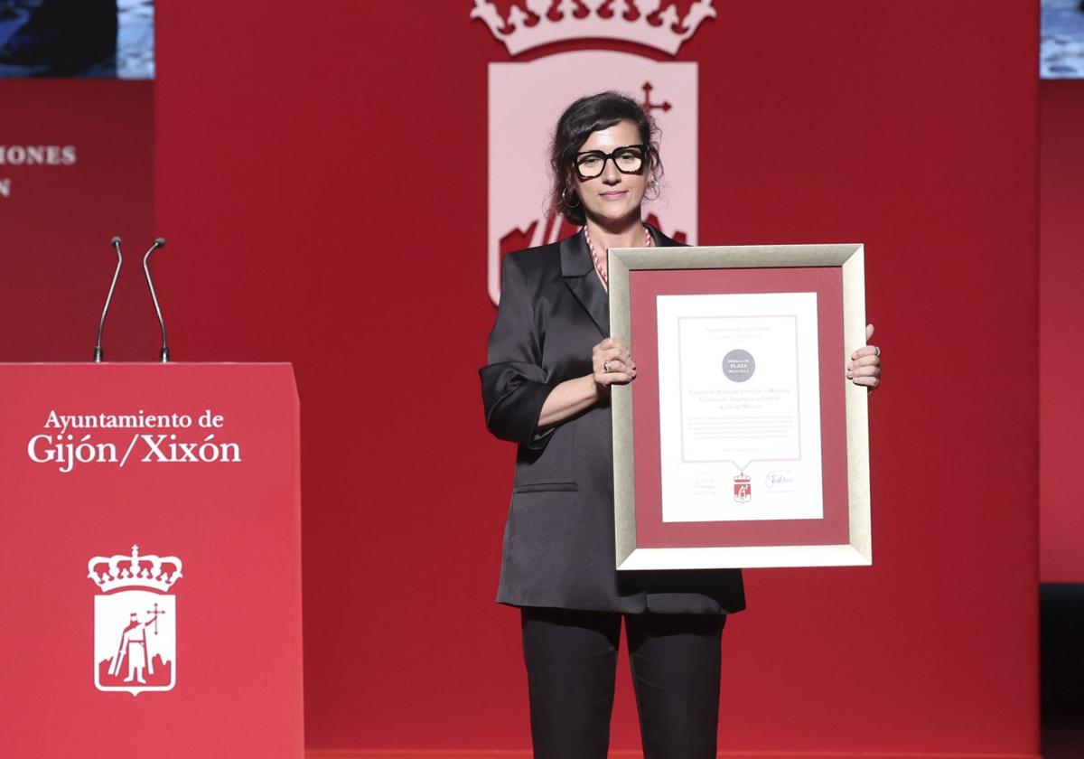 La coordinadora de la red de casas de acogida del Principado, Yoanna Magdalena Benavente, muestra al público la medalla y el diploma de la Casa Malva.