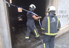 Dos bomberos precintando el bajo incendiado en la calle Maestro Francisco Baragaña, Pola de Siero