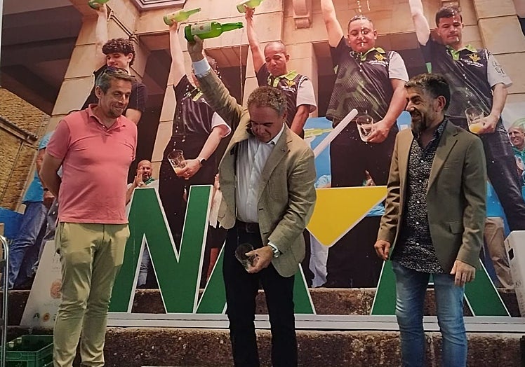 El alcalde de Nava, Juan Cañal, escanciando frente al 'photocall' del pabellón del Principado para su homólogo colungués, José Ángel Toyos, y el presidente de la Mancomunidad de la Sidra, Juan Antonio González.