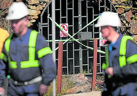Dos mineros pasan ante la boca de la mina de Cerredo, clausurada tras el accidente que costó la vida a cinco mineros.