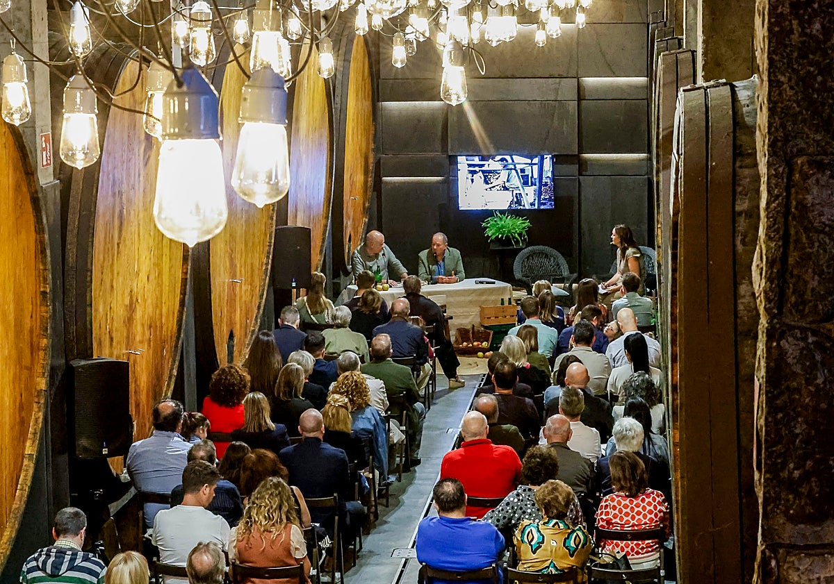 Imagen principal - Samuel Trabanco firma el libro 'Trabanco, 100 años escanciando juntos' en el llagar El Túnel, en una cita familiar en la que conversó con el autor Pachi Poncela, en la foto superior.