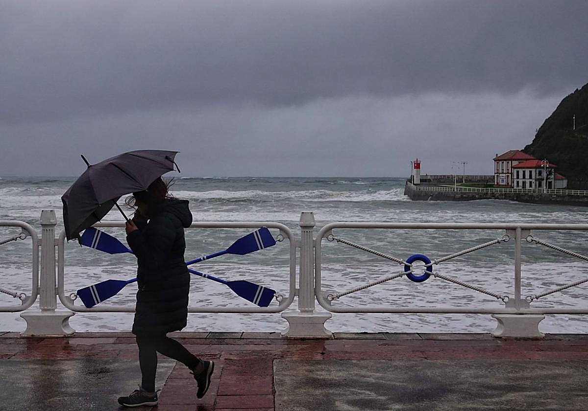 Una mujer pasea bajo la lluvia por Ribadesella.