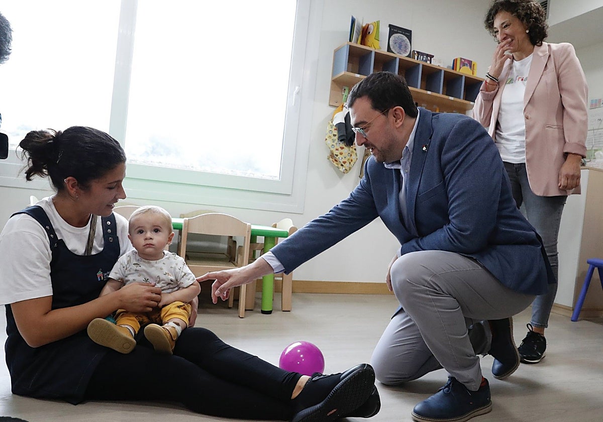 El presidente Adrián Barbón saluda a uno de los niños del centro, en brazos de su profesora.