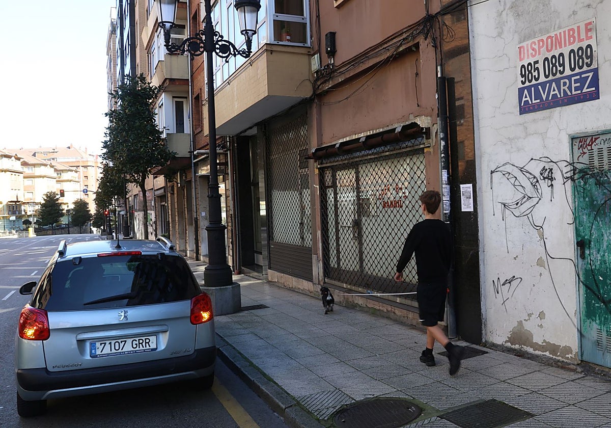 Un joven pasea a su perro por delante de varios bajos comerciales cerrados.