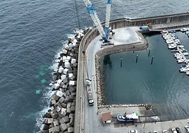 Grúa con una pluma de 78 metros recogiendo uno de los bloques de hormigón de los camiones para su colocación.