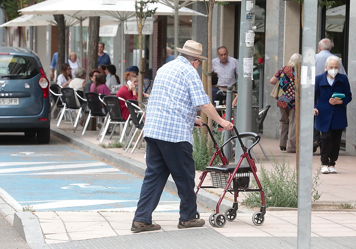 Un hombre camina por la calle apoyado en un andador por sus problemas de movilidad.