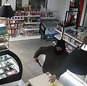 El atracador amenaza con el arma a un empleado para que deje el móvil en el mostrador.