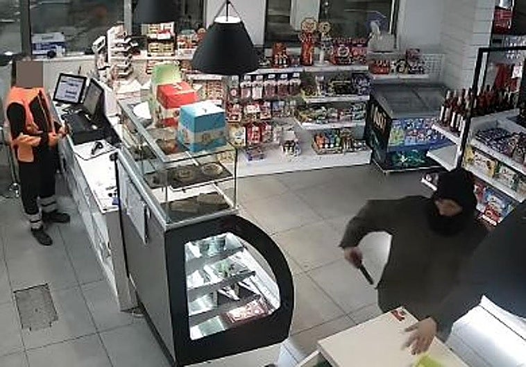 El atracador amenaza con el arma a un empleado para que deje el móvil en el mostrador.