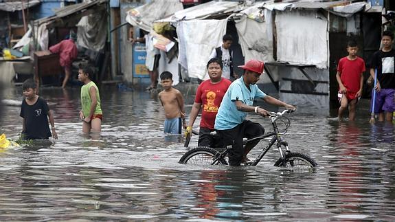 Residentes filipinos intentan protegerse del fuerte viento y lluvia por el paso del tifón Rammasun mientras cruzan una calle inundada en el barrio de chabolas de Tondo. 