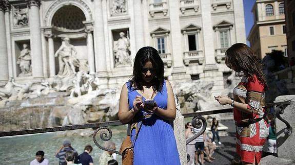 Dos mujeres usan su móvil frente a la Fontana di Trevi. 