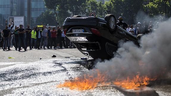 Varios taxistas franceses protestan junto a un vehículo de Uber incendiado.