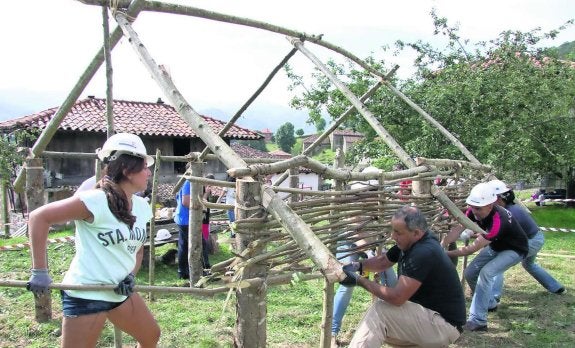 Varias personas colocan las varas de avellano que formarán las paredes de la cabaña neolítica. 