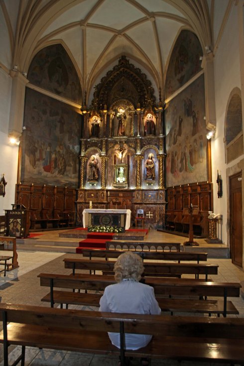 Una mujer ora ante el altar del templo, con el retablo ensalzado por la nueva iluminación.