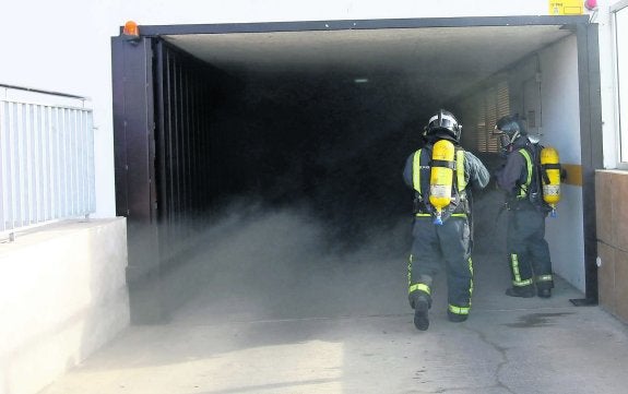 Dos efectivos de bomberos entrando ayer al garaje siniestrado de Pola de Siero. 