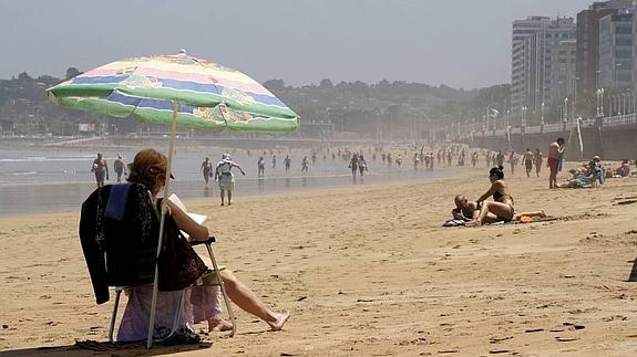 Una mujer se resguarda del sol bajo una sombrilla en la playa de San Lorenzo de Gijón. 