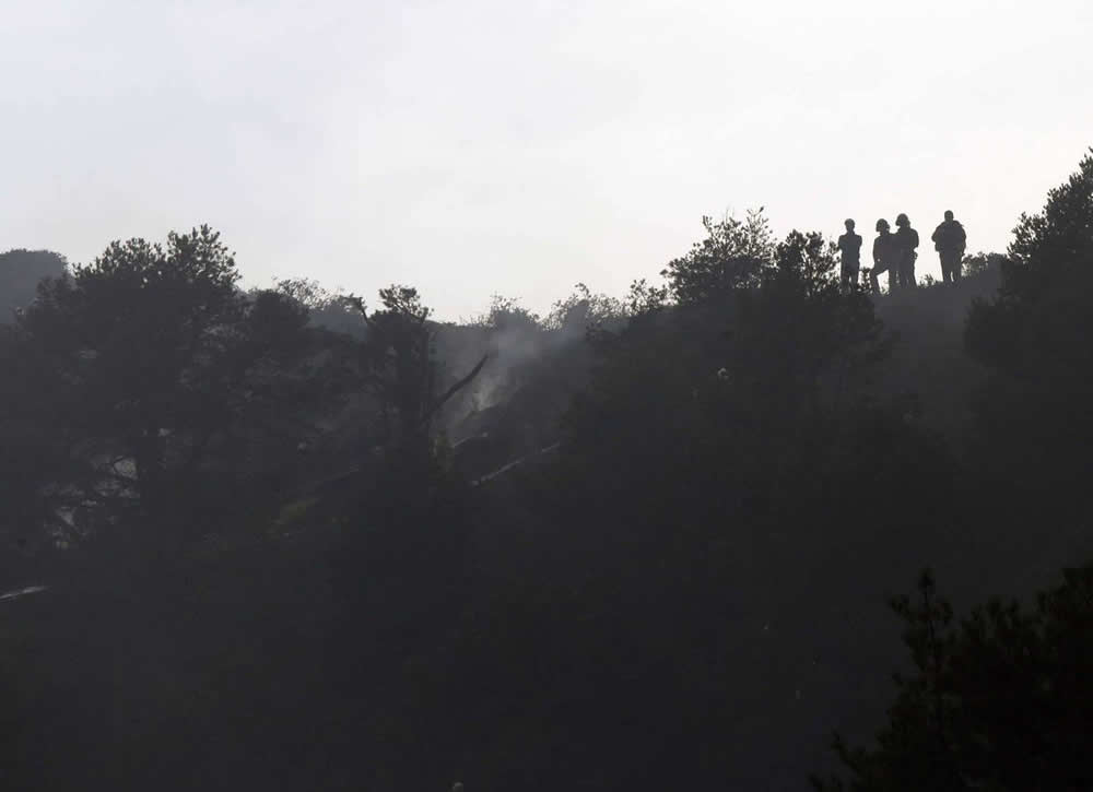 Cuatro efectivos de Bomberos de Asturias observan los restos del helicóptero siniestrado a mediodía de ayer en Parres. 