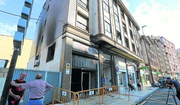 Dos hombres comentan lo sucedido de madrugada en la antigua panadería, que aparece en primer término rodeada por vallas.