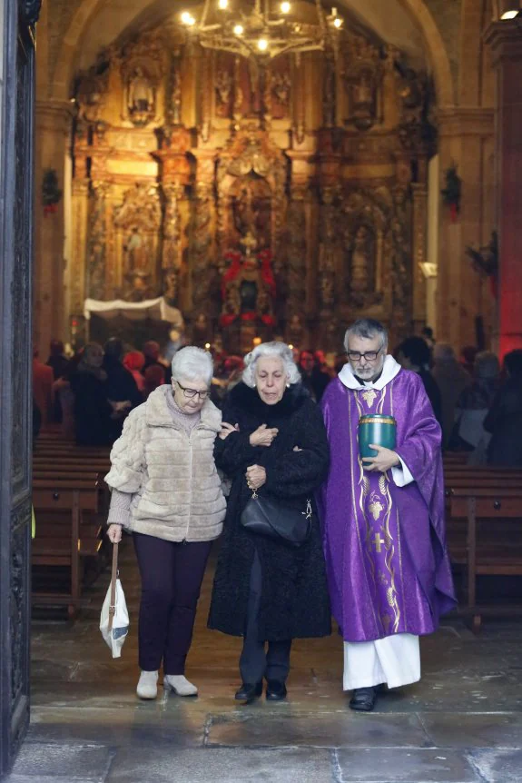 La viuda, en el centro, es acompañada al salir del templo por una familiar de su marido y el párroco Jesús Emilio Menéndez, que porta las cenizas de Parrondo. 