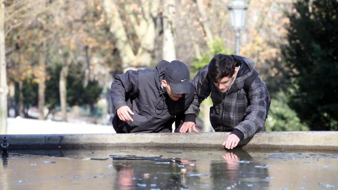 Dos jóvenes comprueban cómo se ha congelado el agua de la fuente del Parque San Francisco. 