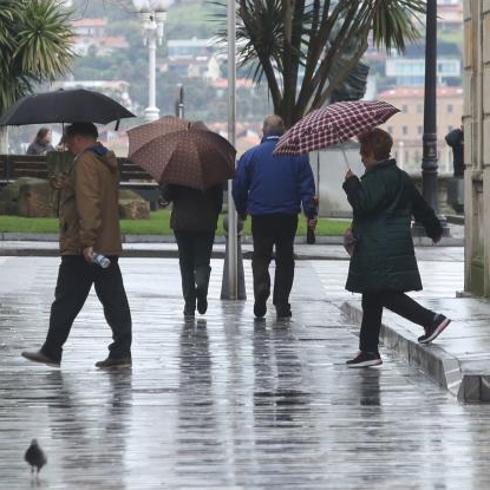 Varias personas caminan con paraguas por el centro de Gijón.