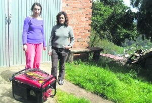 Raquel Iglesias y Ángeles Fernández, vecinas de La Prohida, con el generador eléctrico que utilizan para abastecerse. Al fondo, la mina de Pilotuerto ::                             L. ÁLVAREZ.