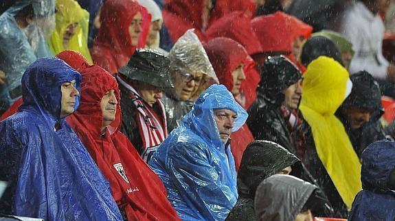 Varios aficionados se protegen de la lluvia.