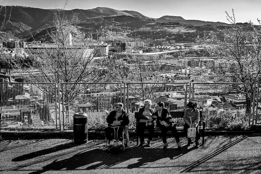 Un grupo de ancianos descansan y dan la espalda a la vista del barrio desde Arangoiti.