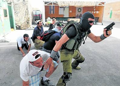 Imagen secundaria 1 - 1. Los asistentes al cursillo atienden las explicaciones de uno de los monitores. 2. Los clientes se agazapan tras un instructor armado.3. Antes de usar fuego real se ejercita con metralletas de madera. 