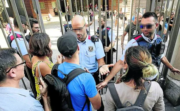 Un mosso trata de impedir sin éxito el acceso de varios ciudadanos a un colegio electoral.