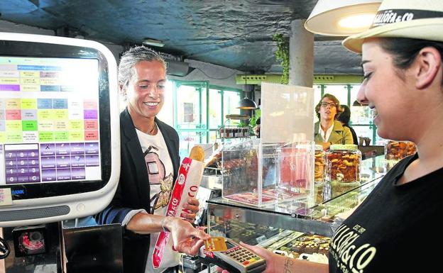 Una clienta paga su barra de pan con tarjeta en el primer día 'sin dinero' de Suances.