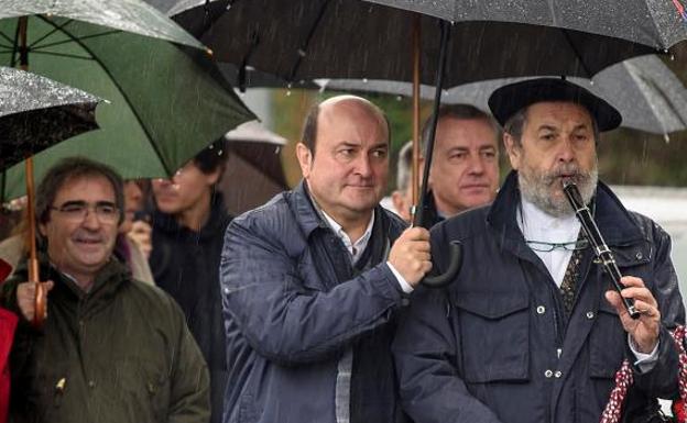 El presidente del PNV, Andoni Ortuzar (c) tapa con su paraguas a un txistulari después de salir de la misa de homenaje a Sabino Arana por el 114 aniversario de su fallecimiento . Detrás de ellos, el lehendakari Iñigo Urkullu.