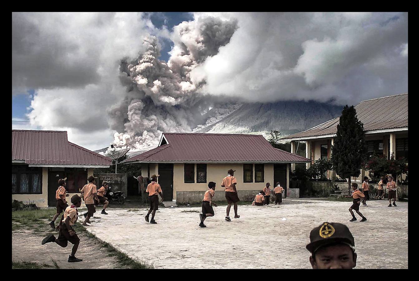 Febrero 2017. Niños de la escuela juegan fuera al lado del volcán Sinabung mientras está en erupción.