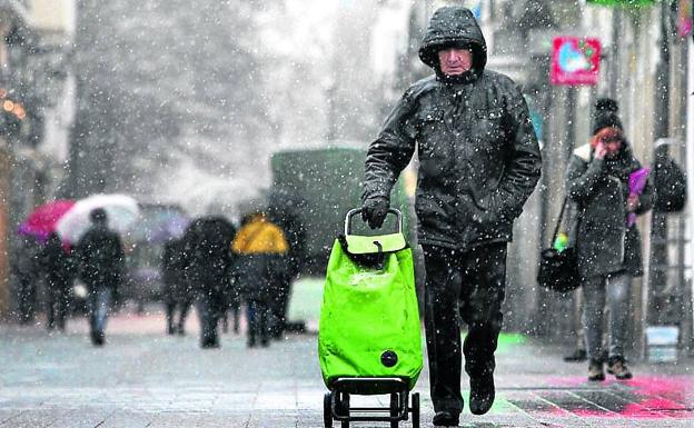 Un hombre empuja un carro de la compra bajo la nieve.