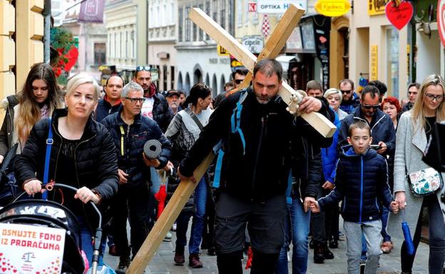 Sasa Pavlic (c) camina con una cruz de madera a sus espaldas acompañado de padres de niños enfermos por las calles de Zagreb. 