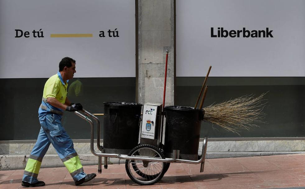 Un barrendero pasa por delante de una sucursal de Liberbank.