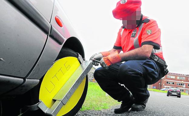 Un agente de la Ertzaintza inmoviliza un vehículo mediante la colocación de un cepo en la rueda.