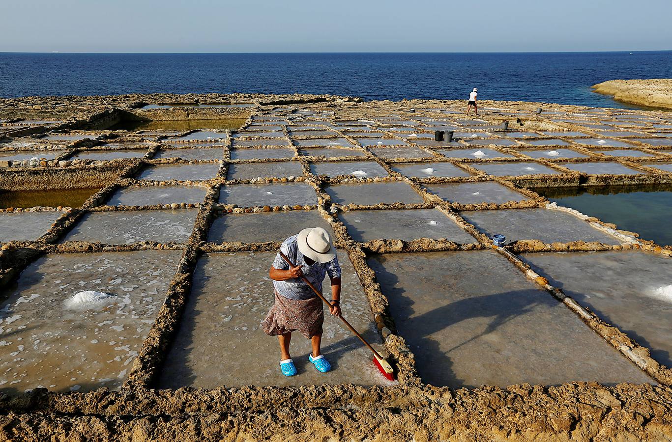 Zebbug, en la isla de Gozo, en Malta, es una pequeña localidad famosa por sus finos encajes; por los olivos, que le dieron el nombre, y por la sal. A ella se dedican numerosos habitantes que, como Josephine Xuereb y Rosa Cini (en las fotos), la tratan y almacenan en salinas excavadas en roca y en paneles de evaporación, que se extienden a lo largo de la costa, de la misma forma que hicieron otras generaciones desde hace más de 350 años. 