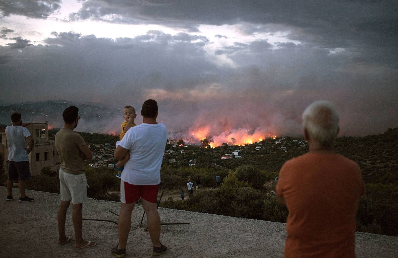 Un grupo de personas observa un incendio forestal en la ciudad de Rafina, cerca de Atenas.